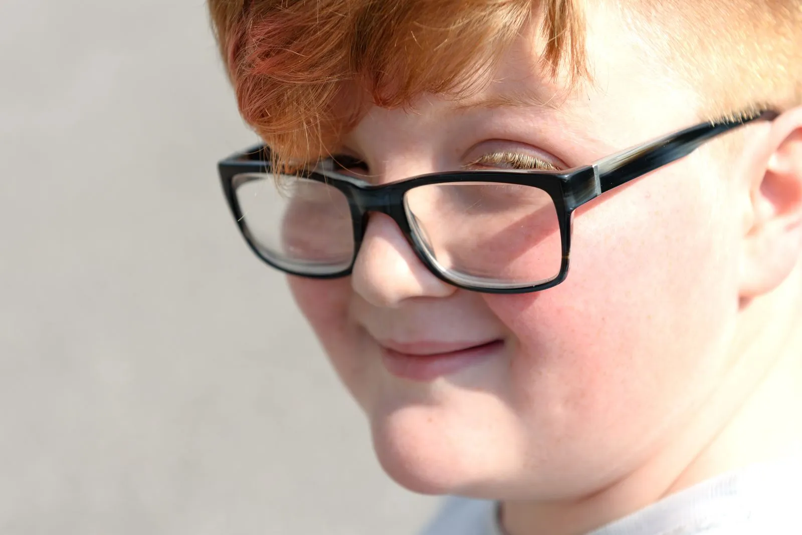 Close-up of a smiling young boy with red hair and eyeglasses.